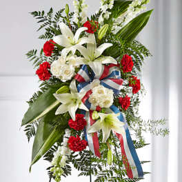 Standing floral spray with white lilies, red carnations, and ribbon on an easel