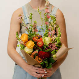 Person holding a colorful mixed bouquet wrapped in brown paper