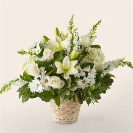 White lilies, roses, and daisies arranged in a woven basket with lush foliage