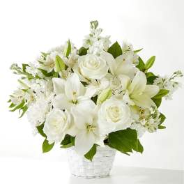 White lilies and roses arranged with other white blooms in a white woven basket
