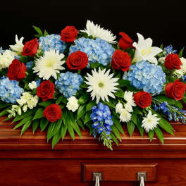 Red, white, and blue casket spray on a polished wooden casket