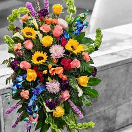 Tall multicolored standing spray with sunflowers, roses, orchids, and other blooms on a metal easel