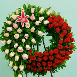Standing wreath of red and pale roses with a pink lily on a metal easel.