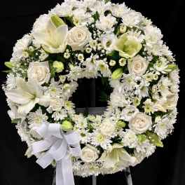 Standing white funeral wreath of roses, lilies, and chrysanthemums with a bow on a metal easel