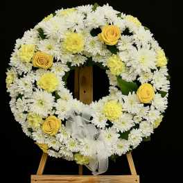 White and yellow floral wreath on a wooden easel with a ribbon bow