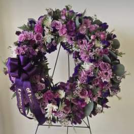 Purple floral wreath on a black stand with a ribbon bow