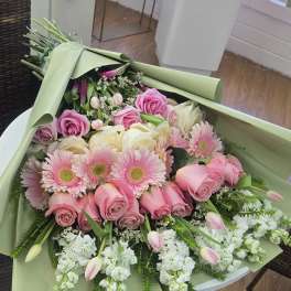 Large bouquet of pink roses, gerbera daisies, and white flowers wrapped in pale green paper