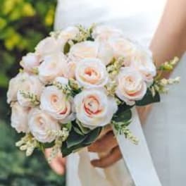 Bride holding a bouquet of pale pink roses with white ribbon