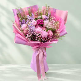 Pink and lavender bouquet wrapped in pink paper with a ribbon tie