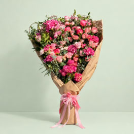 Large bouquet of pink flowers wrapped in brown paper with a pink ribbon