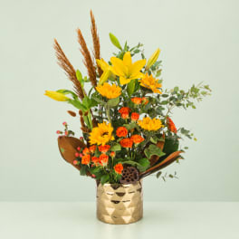 Yellow lilies and orange roses in a gold vase