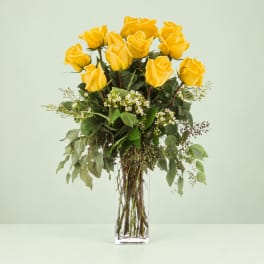 Yellow roses in a clear glass vase with mixed greenery