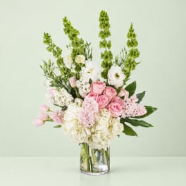 Pink and white bouquet in a clear glass vase with tall green spikes
