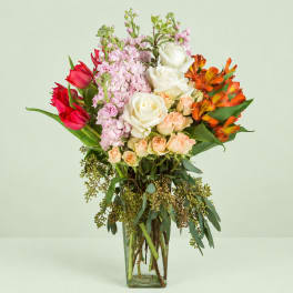Mixed bouquet of roses, tulips, and orange alstroemeria in a clear glass vase