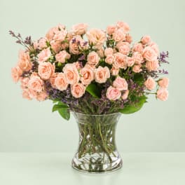 Pink roses in a clear glass vase with purple filler flowers