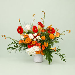 Bright mixed bouquet in a white vase with red, orange, and white blooms