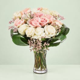 Pink and white roses in a clear glass vase with broad green leaves