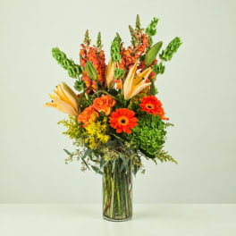 Orange and yellow mixed flowers arranged in a clear glass vase