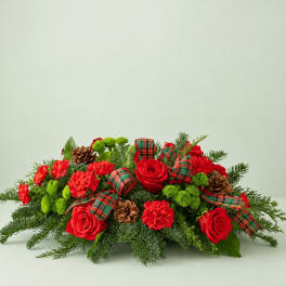Low holiday arrangement with red roses, red carnations, and plaid ribbon