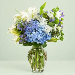 Blue hydrangeas and white lilies in a clear glass vase