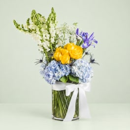 Bouquet of yellow roses, blue hydrangeas, and purple irises in a glass vase