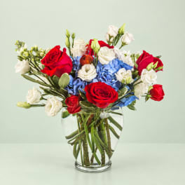 Red roses and white lisianthus in a clear glass vase with blue hydrangeas