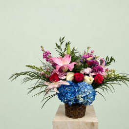 Mixed bouquet with pink lilies, roses, and blue hydrangeas in a woven basket