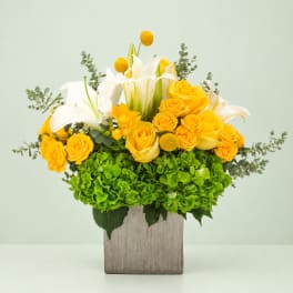 Yellow roses and white lilies in a square wooden vase