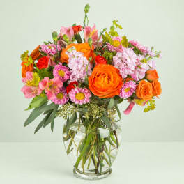Mixed bouquet of orange, pink, and red flowers in a clear glass vase
