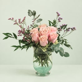 Pink roses in a clear glass vase with purple filler flowers