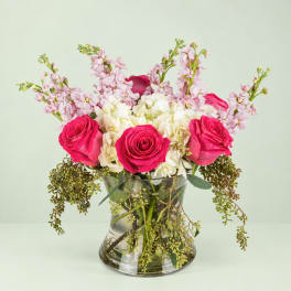 Pink roses and white hydrangeas in a clear glass vase with trailing greenery