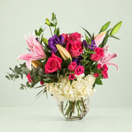 Pink roses and lilies with purple blooms in a clear glass vase