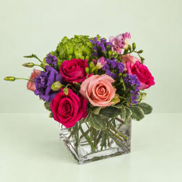 Mixed roses and purple flowers arranged in a clear glass cube vase