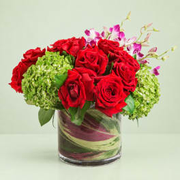 Red roses with green hydrangeas and pink orchids in a glass vase