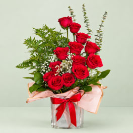 Red roses arranged in a clear glass vase with pink wrap and ribbon