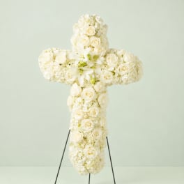 White floral cross on a stand with roses and lilies