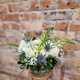 White rose bouquet with blue thistle in a glass vase