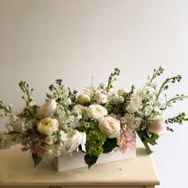 Low centerpiece of white and blush roses with green hydrangea in a white rectangular vase