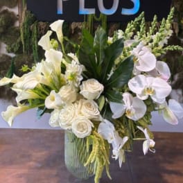 White floral arrangement with calla lilies, roses, and orchids in a glass vase