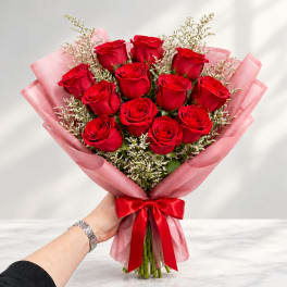 Bouquet of red roses wrapped in pink paper with a red ribbon
