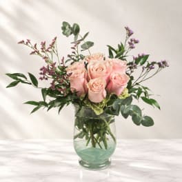 Pink roses arranged in a clear glass vase with purple filler flowers