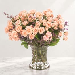Peach spray roses in a clear glass vase with purple filler flowers