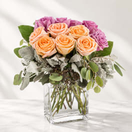 Peach and purple roses arranged in a clear square vase