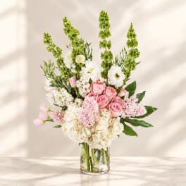 Pink roses and white flowers in a clear glass vase with tall green spikes