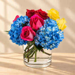 Bouquet of blue hydrangeas and pink, red, and yellow roses in a clear glass vase