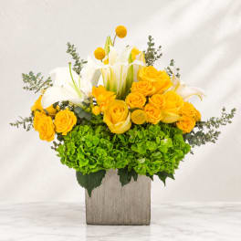Yellow roses and white lilies in a square vase with green hydrangeas