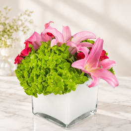 Pink lilies and roses in a square glass vase with bright green hydrangeas