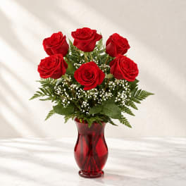 Red roses arranged in a red glass vase with baby's breath