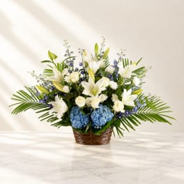 White lilies and roses in a wicker basket with blue hydrangeas