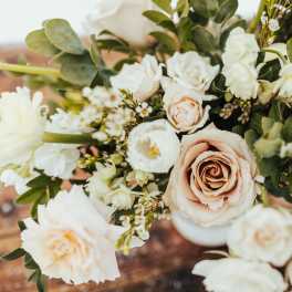 Arrangement of blush roses and white flowers in a white vase on a wooden surface